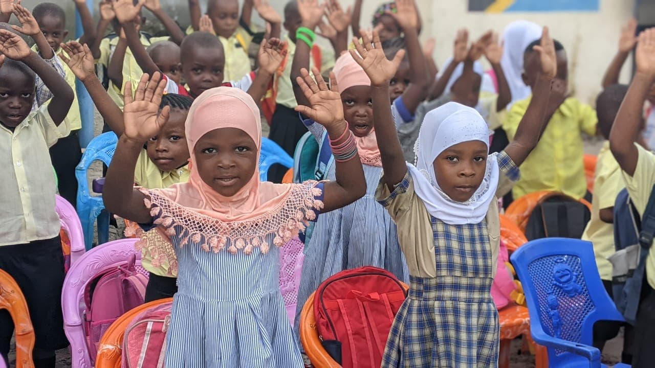 Amosi Schools young learners raising their hands during a school activity